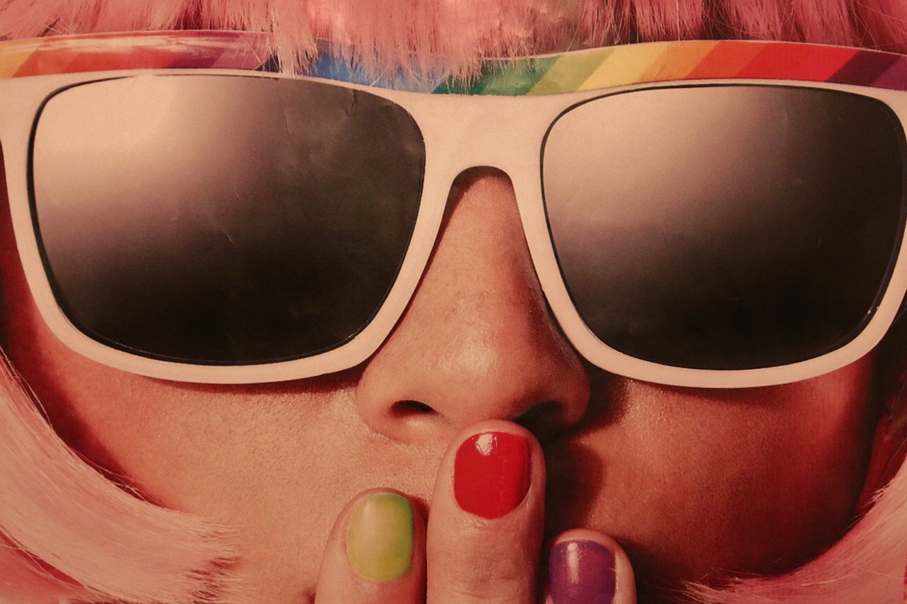 Close up of a woman in a colorful wig wearing sunglasses covering her mouth with her hand