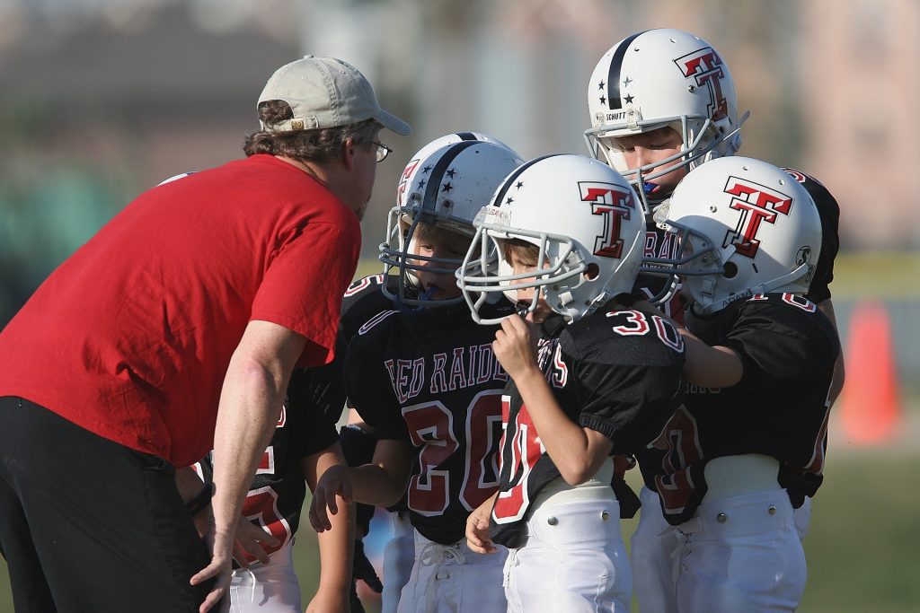 Coach talking to four young football players on the field