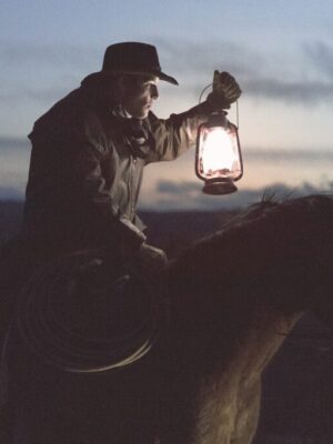 Cowboy on a horse at dusk holding a lantern